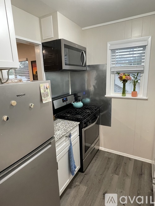 A small kitchen with a refrigerator, microwave, oven, and a window with flowers on the sill.
