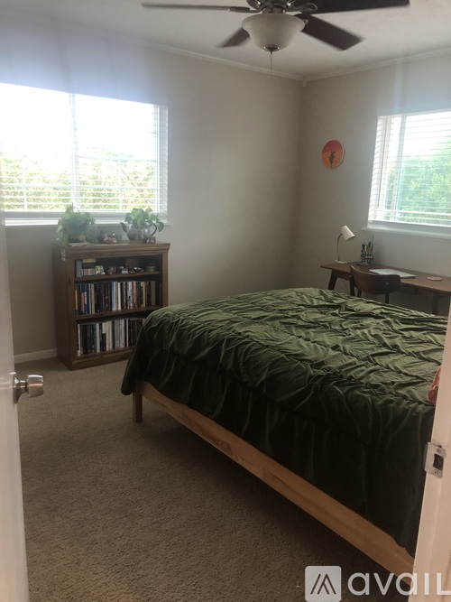 A bedroom with a bed, a desk, a bookshelf, and a ceiling fan.