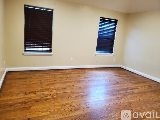 A room with wooden flooring and two windows with blinds.