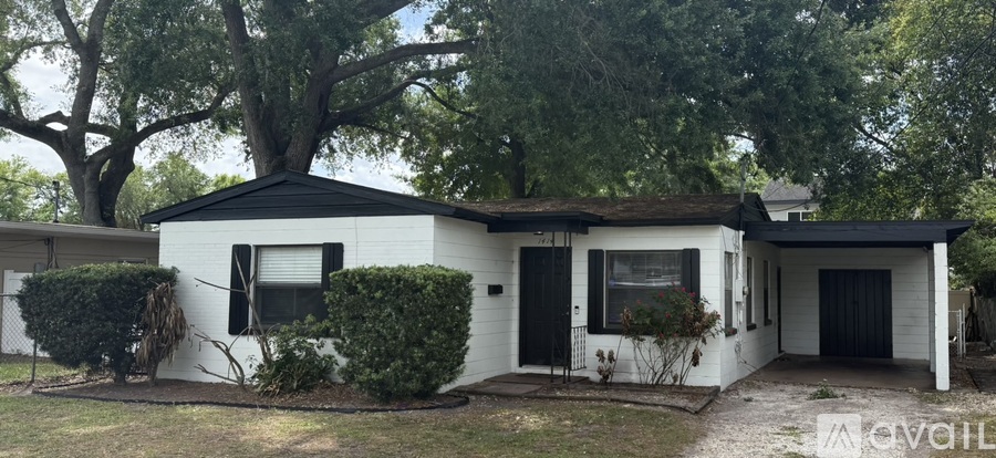 A white house with a black roof and a black door is surrounded by trees.