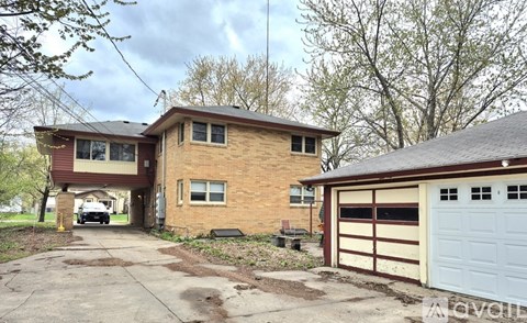 A two-story house with a garage is surrounded by trees.