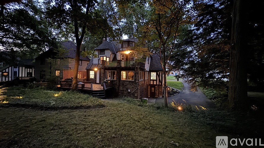 A large house with a lit up porch is surrounded by trees.
