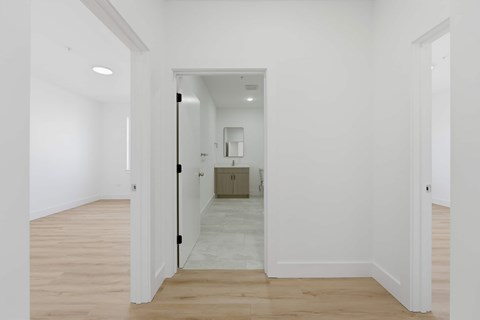 A white hallway with a black door and a mirror on the wall.