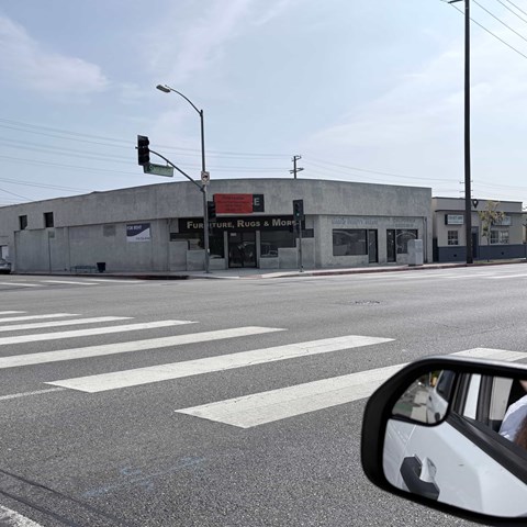 A car's side mirror is visible in the foreground of a street with a building that has a sign for Furniture, Rugs & More.