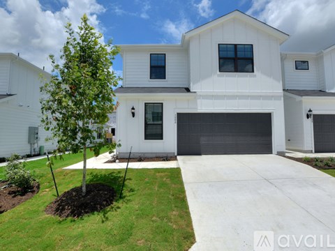 A white house with a grey garage door and a tree in front.