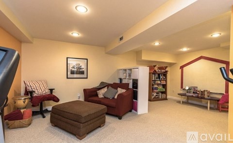A living room with a red couch, a brown ottoman, and a bookshelf filled with books.