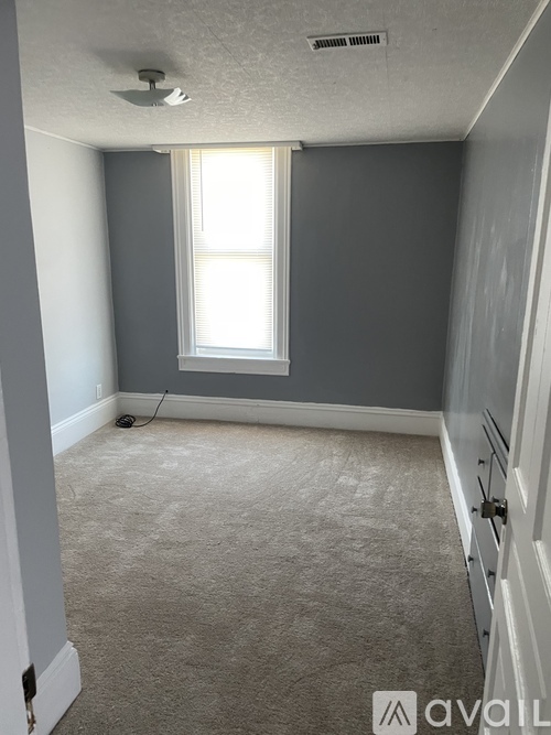 A room with a carpeted floor and a window with blinds.