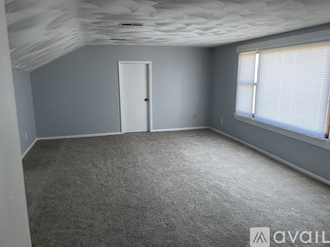 A room with a carpeted floor, a door, and a window with blinds.