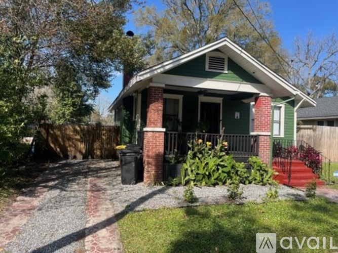 A small green house with a porch and a red brick pillar.