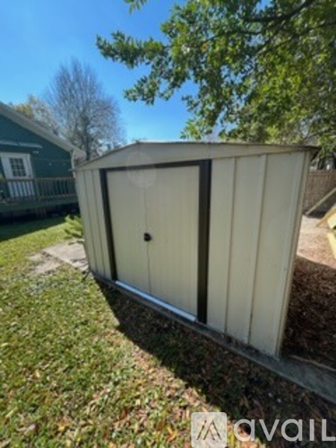 A small, white, metal shed with a door and windows is situated in a grassy area.