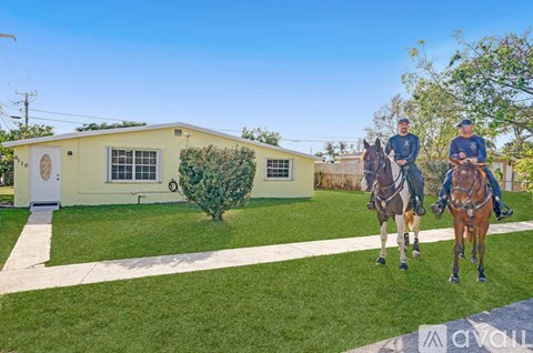 Two people riding horses in front of a yellow house.