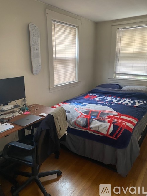 A bedroom with a bed, desk, chair, and a window with blinds.