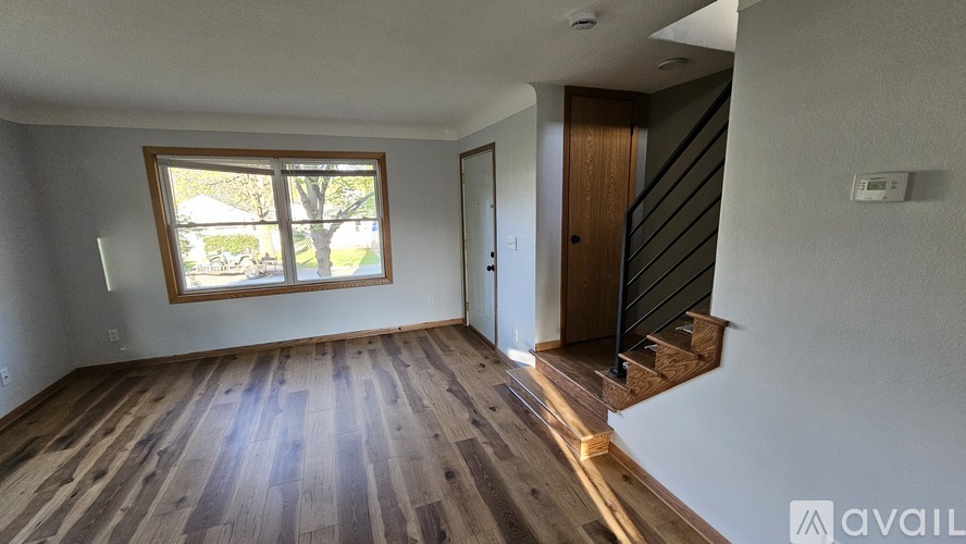 A room with wooden flooring and a window showing a view of a house.