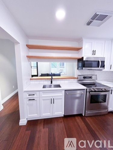 A kitchen with white cabinets and a wooden shelf above the sink.
