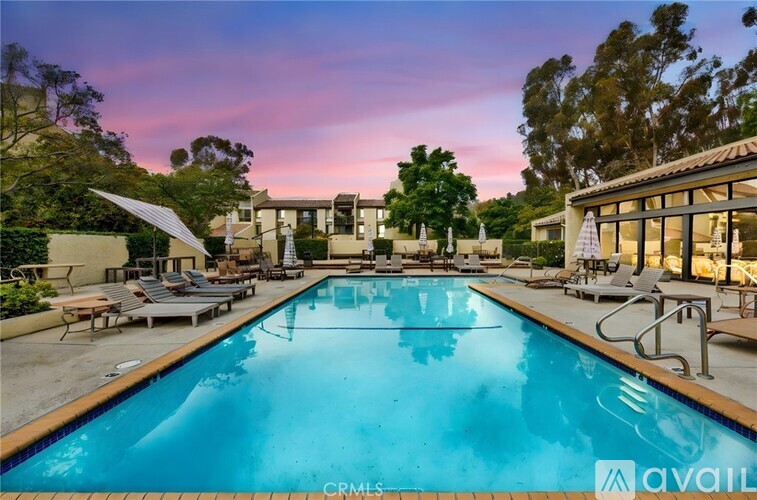 A large pool with a sun lounger and a building in the background.