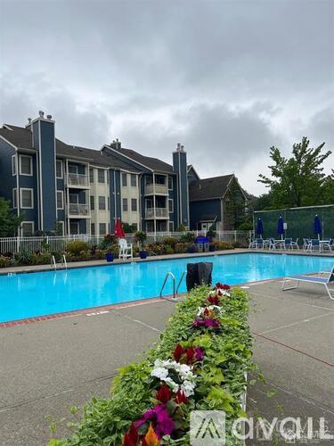 A pool area with a building in the background and a flower bed in the foreground.