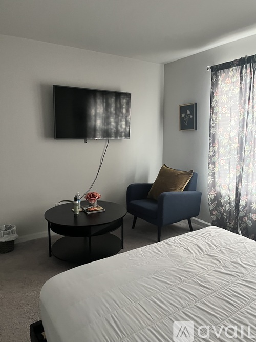 A bedroom with a bed, a table with a vase and a bottle, and a chair with a pillow.
