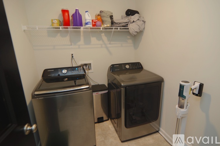 A kitchen with a stainless steel refrigerator and oven, a microwave, and a shelf with various items on it.