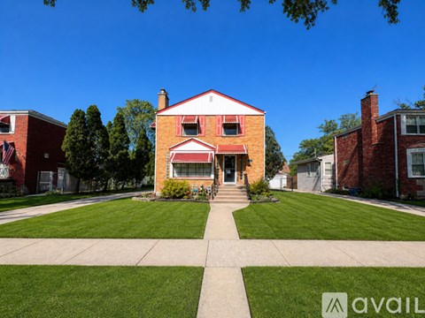 A house with a red brick exterior and a white trim is surrounded by a well-manicured lawn.