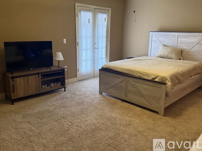 A bedroom with a bed, a television, and a carpeted floor.