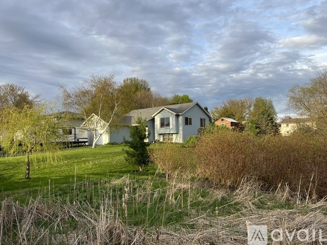 A house with a white fence is surrounded by grass and trees.