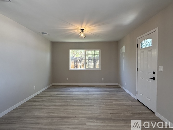 A room with wooden flooring and a window with a view of a fence and trees.