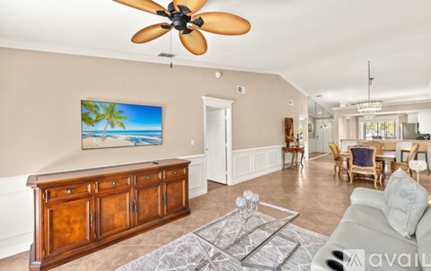 A living room with a ceiling fan and a painting of a beach scene on the wall.