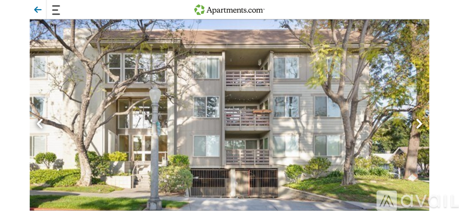 Apartment building with a balcony and trees in front.