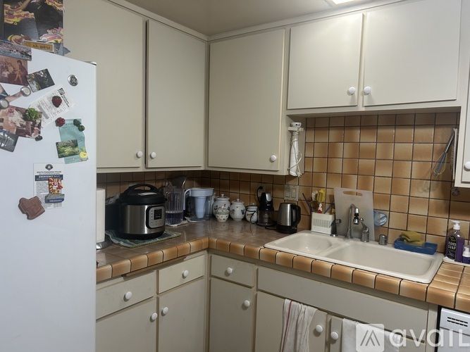 A kitchen with a white fridge, brown tiled backsplash, and white cabinets.