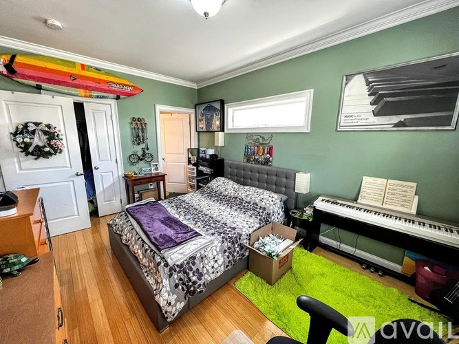 A bedroom with a bed, a piano, and a surfboard on the wall.