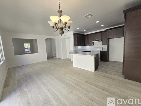 A spacious kitchen with a wooden floor and a chandelier hanging from the ceiling.