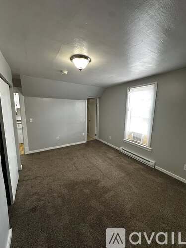A room with a carpeted floor and a window with white curtains.
