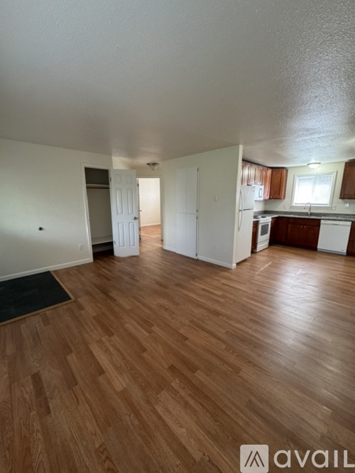 A room with wooden flooring and a kitchen area in the background.
