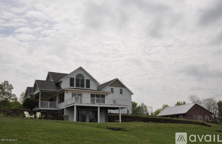 A large white house with a balcony and a red barn in the background.