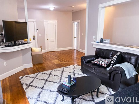 A living room with a black leather couch and a television on a stand.