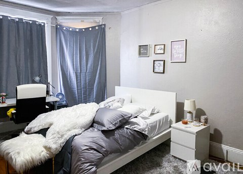 A bedroom with a white bed, grey bedding, and a white nightstand with a lamp.