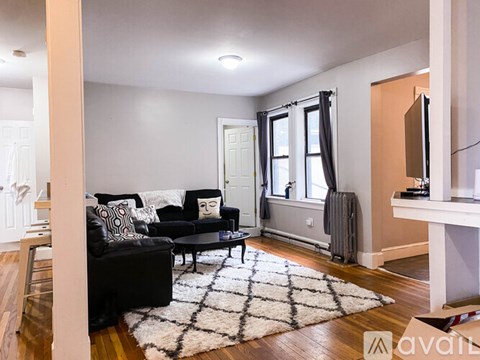 A living room with a black couch and a white rug.