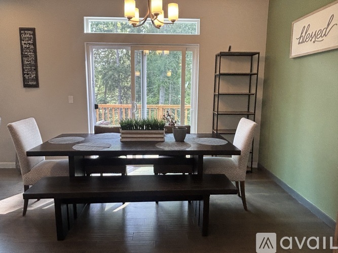 A dining room with a table set for two and a view of a deck outside the window.