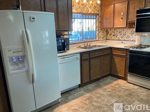 A white refrigerator stands in a kitchen with wooden cabinets and a tiled backsplash.