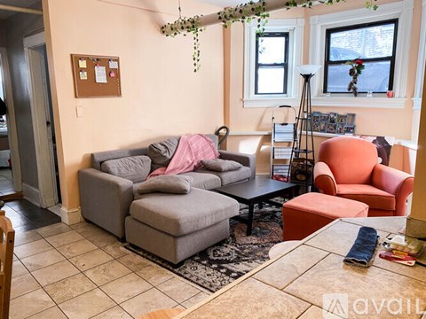 A living room with a grey couch and a pink blanket on it.