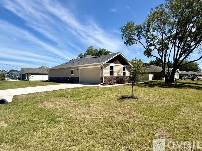A house with a brown roof and a white garage door is surrounded by a grassy lawn.