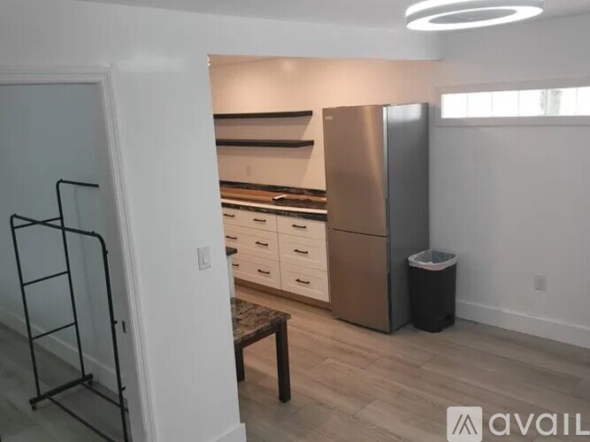 A kitchen area with a refrigerator, a table, and a trash bin.