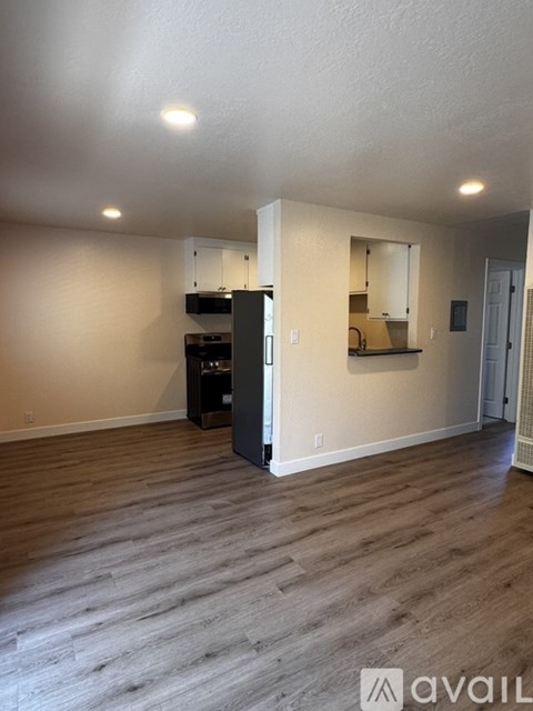 A kitchen area with a black refrigerator and wooden flooring.