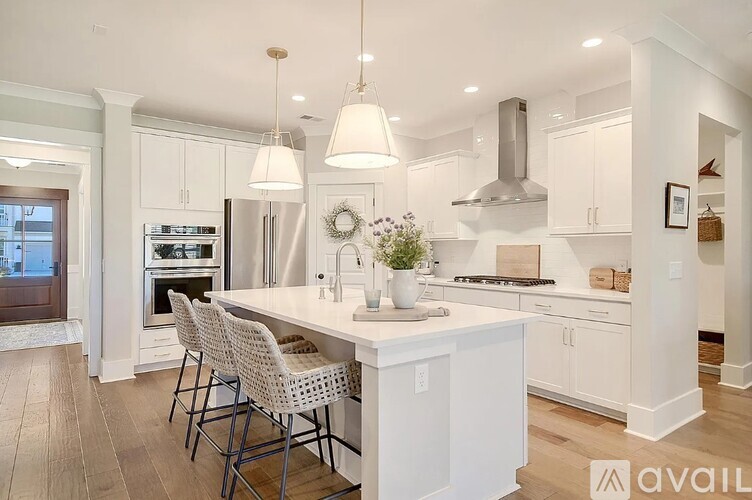 A kitchen with white cabinets and a large island with chairs around it.