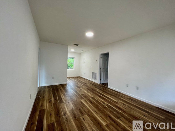A room with wooden floors and white walls, with a door on the right and a window on the left.
