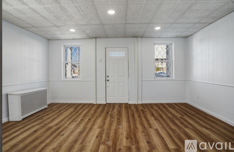 A room with wooden floors and white walls, featuring a white door and two windows with stained glass.