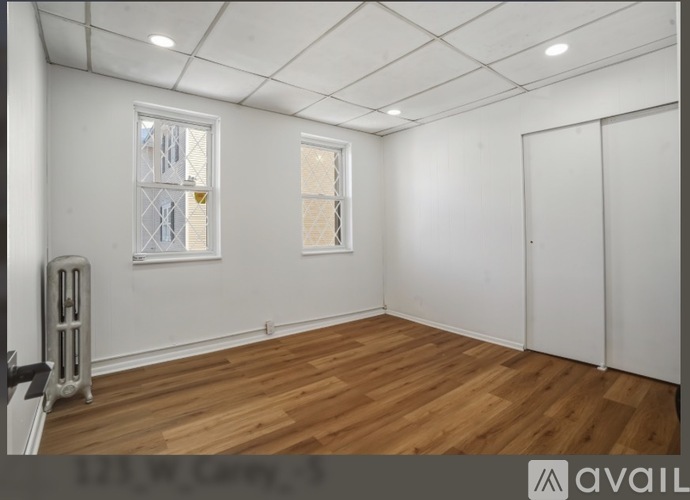 A room with wooden flooring and white walls, featuring a window with a view of a building outside.