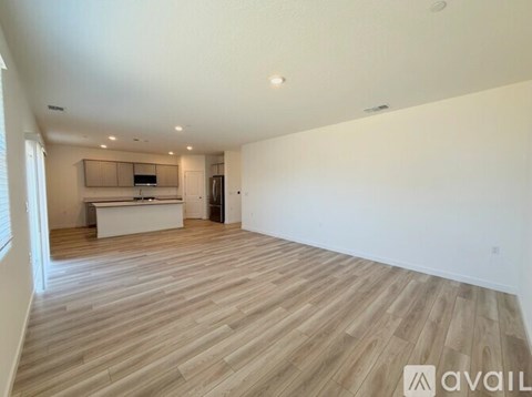 A spacious room with wooden flooring and a kitchen area in the background.