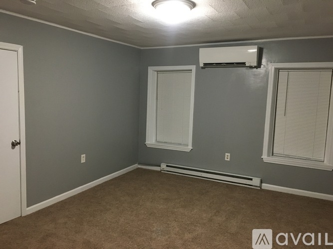 A room with a carpeted floor, a window with blinds, and a door.