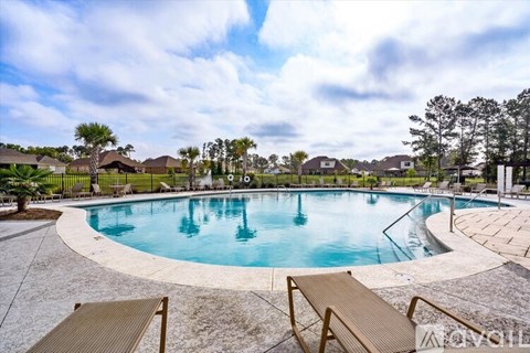 A large outdoor swimming pool surrounded by a concrete patio and deck chairs.